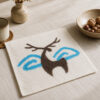 Carré écru à motif de cerf brun et formes bleues sur une table